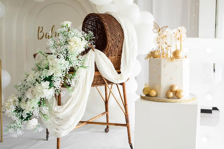 Baby shower styling with a cane bassinet, white blooms and cake