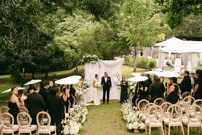 Garden ceremony beneath the trees with guests holding parasols