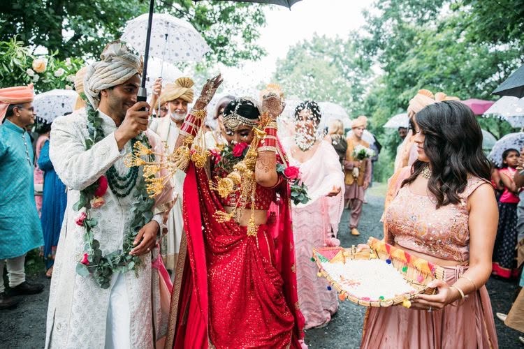 The couple walking beneath umbrellas as guests welcome them