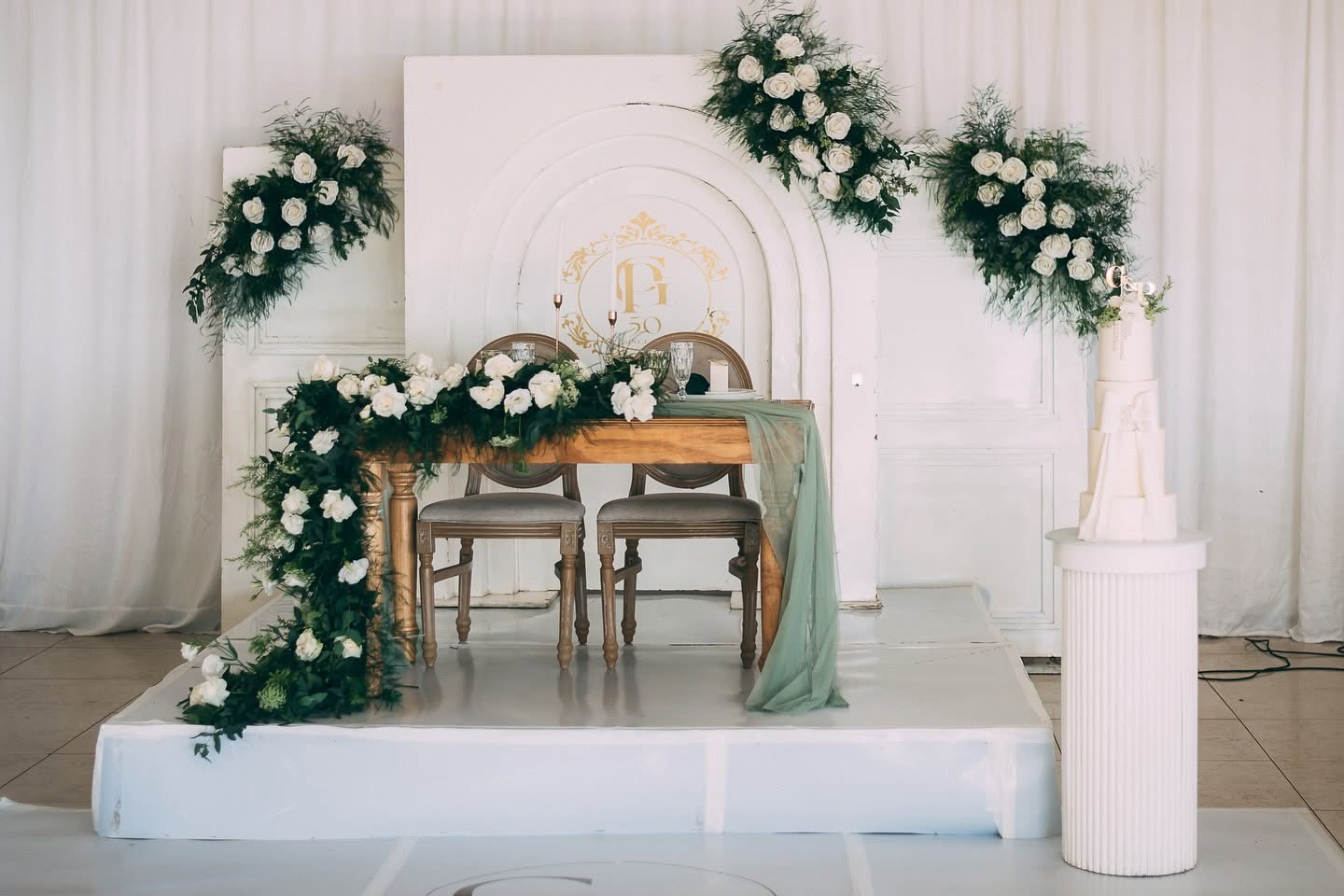 Sweetheart table with white roses, sage runner and tiered cake